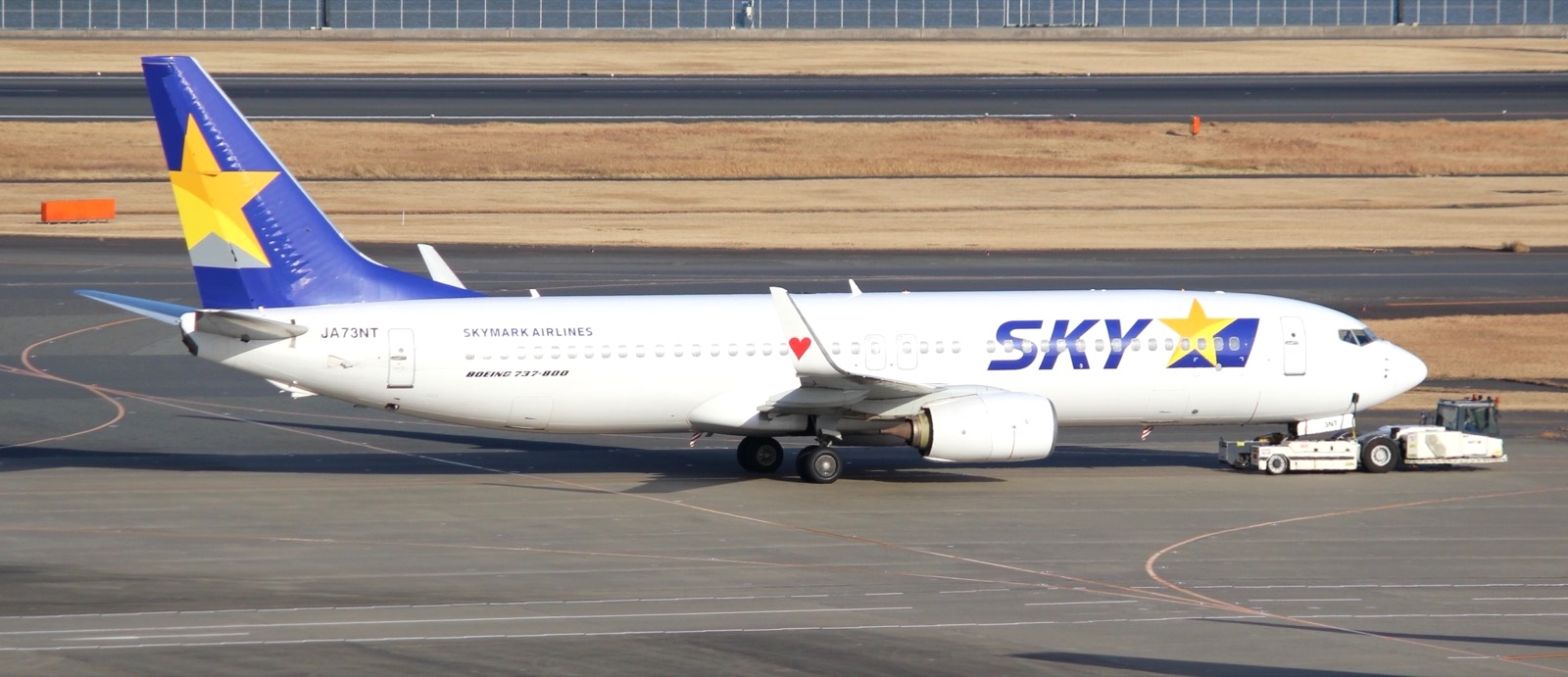 スカイマークのボーイング737-800、JA73NTを横から撮った写真。翼の先にウイングレットが立ち上がっていて、赤いハートが描かれている。胴体の後ろにJA73NTの文字が見える