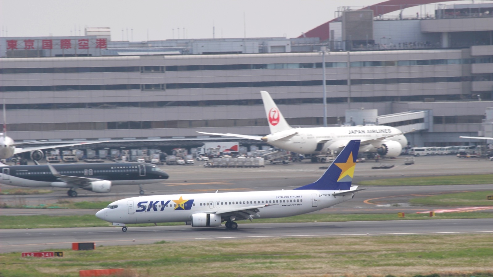 羽田空港を走るスカイマークのJA737N。奥に黒い塗装のスターフライヤーの機体と、JALのボーイング787、東京国際空港のターミナルが写っている
